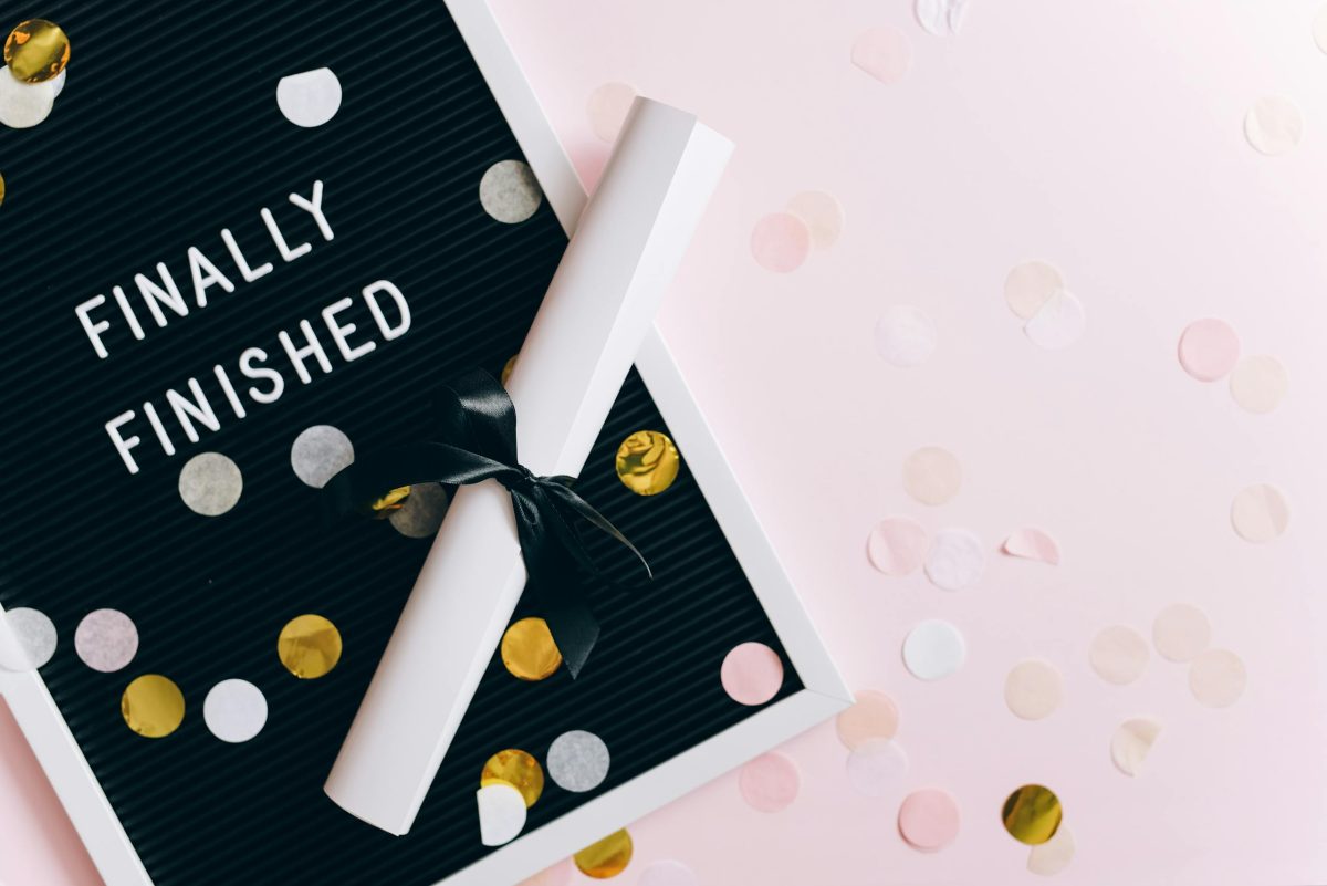 A graduation scene with a diploma and confetti on a letter board reading 'Finally Finished.'